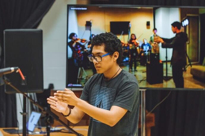 Puentes Telemáticos / Telematic Bridges 2017, student Cristobal Gallardo leading conduction with performers in California, in collaboration with remote student ensemble in Colombia (on screen)--Photo by Will Tee Yang